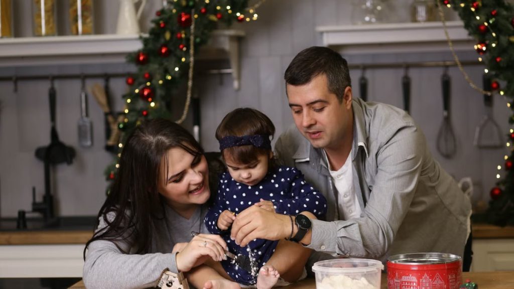 A joyful family of three baking together in a festive kitchen setting.